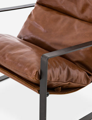 Close-up of the right metal arm of the brown leather Marlyne sling-back accent chair with black metal frame