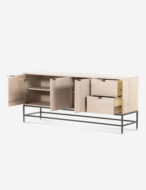 The three opened doors and two opened drawers of the Rosamonde natural wood sideboard with brown leather pulls and a metal base