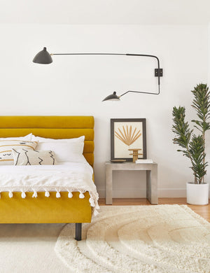 The Gin indoor and outdoor concrete side table sits in a bedroom with a golden linen bed, a floral wall art, and a white plush rug