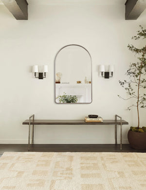The Shashenka arched wall mirror with silver frame hangs in a room with beamed ceilings above a metal bench