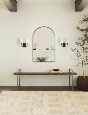 The Shashenka arched wall mirror with golden frame hangs in a room with beamed ceilings above a metal bench