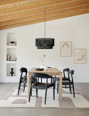 Five Black Ida Dining Arm Chairs sit around a rectangular wooden dining table beneath a black jute chandelier and wooden ceiling