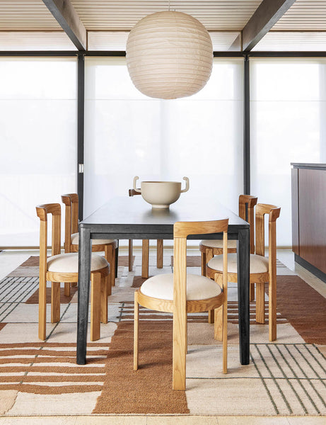 #color::black #size::82-W | The Reese black mango wood rectangular dining table sits in a bright dining room surrounded by sculptural oak wood dining chairs atop a brown and neutral patterned rug.