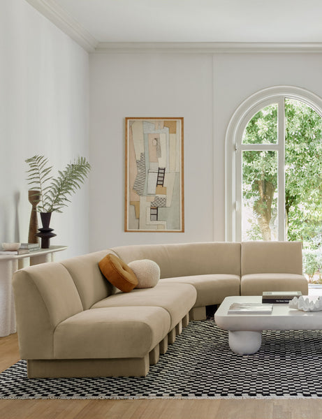 #showall::39705710133347 | The Lena right-facing beige velvet sectional sofa with upholstered beam legs sits in a sculptural living room with a rounded coffee table and a boucle accent chair atop a black and white checkered rug.