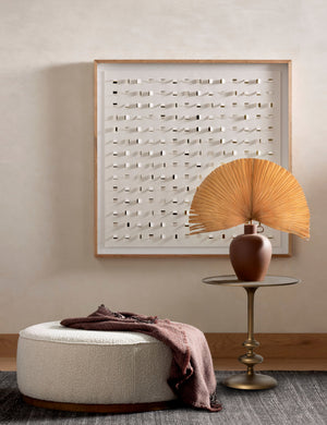Caratto round matte brass finish metal side table styled next to a large round ottoman and modern wall artwork.