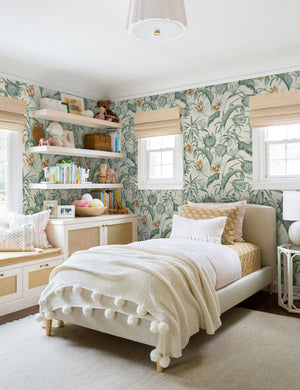 Green-toned Tropical Wallpaper by Rylee + Cru is in a children's bedroom with a pom-pom throw blanket and a shelf lined with children's toys