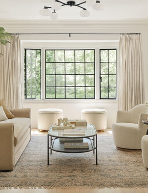 The Solange antique bronze branching 6-light semi flush mount light is mounted in a living room with two white boucle accent chairs, a persian rug, and a beige linen sofa