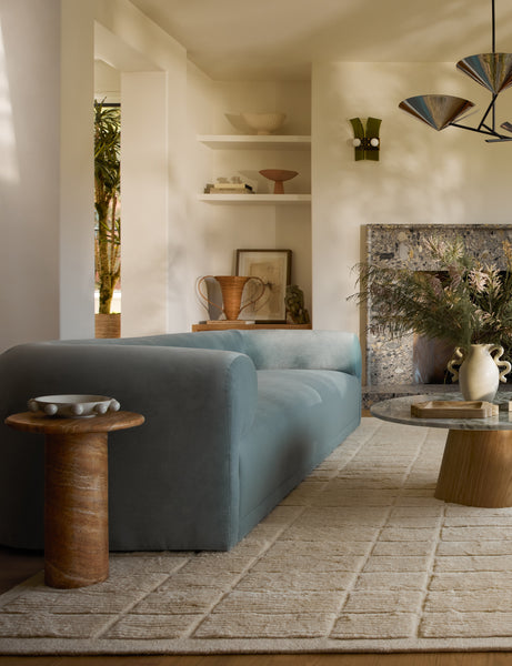 #color::Canyon-Faux-Travertine | Mona round stone drink table styled next to a blue velvet sofa.