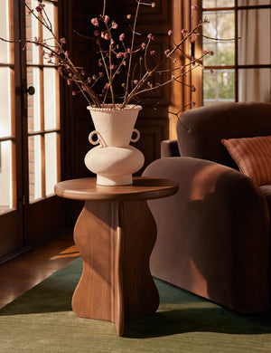The Telle wavy leg solid wood round side table by Aimee Song with a ceramic vase on top styled next to an accent chair