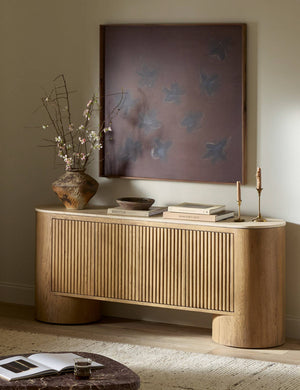 The Cagney sculptural vertical reeding media console styled with large scale artwork and a vase filled with botanicals.