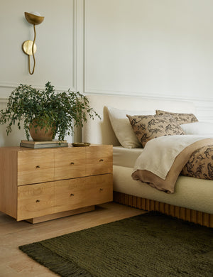 Kukka modern wavy arm wall sconce in brass hung above a nightstand in a bedroom