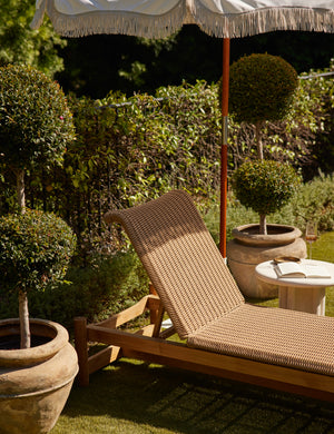 Gally wicker and teak outdoor chaise styled with a round cement outdoor side table and umbrella with a fringe.