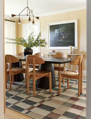 The marli rug lays in a dining room under a rectangular black wooden dining table and sculptural wooden dining chairs