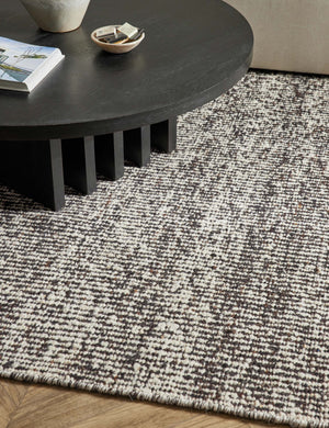Close up of the Taos espresso rug laying in a living room under a round coffee table and an ivory sectional