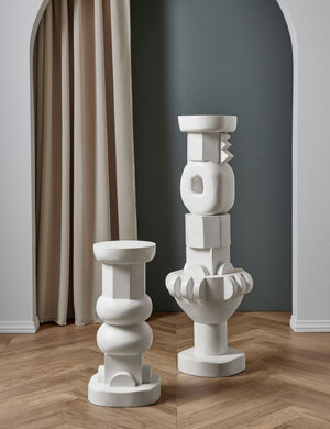 The Toivo short and tall pedestals stand next to each other in a room with a curtain backdrop and chevron floors