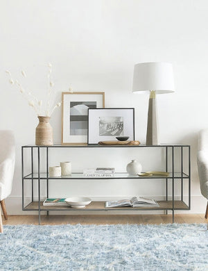 The Asher console table filled with decorative objects sits against a white wall in a room with a blue rug