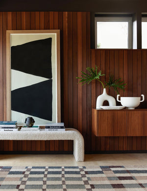 The marli rug lays in a retro room with wood-paneled wall, a geometric wall art, and a cream boucle bench