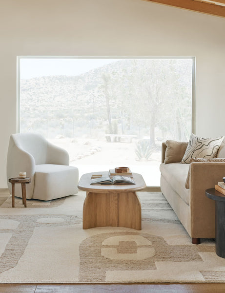#showall::39840600883299 | The Tobi natural linen swivel chair sits atop a natural and ivory patterned carpet in front of a large window with a desert view