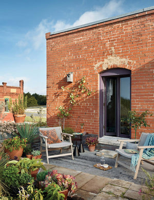 Two Ylva Natural Indoor / Outdoor Accent Chairs sit on a rooftop outdoor space with a brick wall and various plants