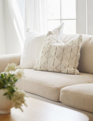 The Norala solid white handmade square throw pillow sits on a natural linen sofa with a white throw pillow behind it