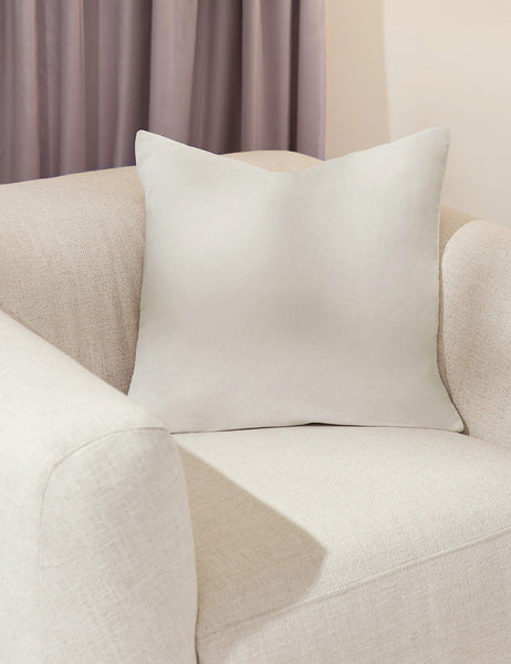 #color::oyster #style::square  #fill type::with-feather-down-insert  #fill type::pillow-cover-only |   Charlotte oyster white square velvet pillow sits on a white accent chair with a purple curtain in the background