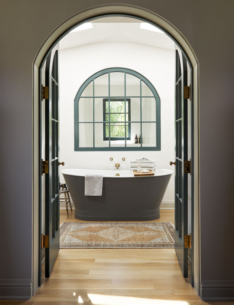  #size::3--x-5- | The Kate desert palette geometric floor rug sits in a bathroom in front of a black bathtub behind a black-framed arched entrance.