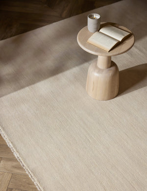 The Heritage ivory rug lays under a light wooden round side table with a lit candle and open book atop it