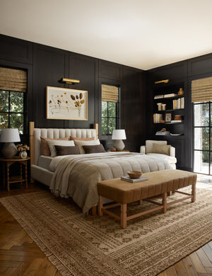  The Ambleside camel linen bench sits atop a patterned rug in a room with accented black wooden walls and a natural linen bed