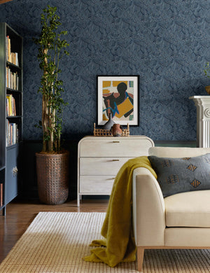 The Indigo woven cotton boho and folk-inspired lumbar pillow with a wool front sits on a beige linen sofa in a living room with indigo patterned walls and colorful decor accents