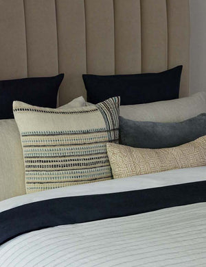 The Kisha natural-toned lumbar throw pillow sits on a beige velvet framed bed with blue and ivory linens