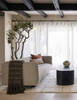 The Pismo dark gray pure wool throw blanket with fringed ends lays on a gray linen sofa in a living room with a cream plush rug