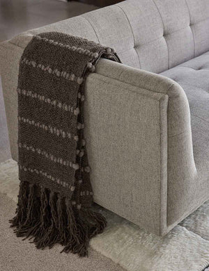 The Pismo dark gray pure wool throw blanket with fringed ends lays on a gray linen sofa in a living room with a cream plush rug