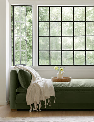 The Trestles white chunky knit throw by pom pom at home lays atop sage velvet bench in a nook with a cork tray and white vase