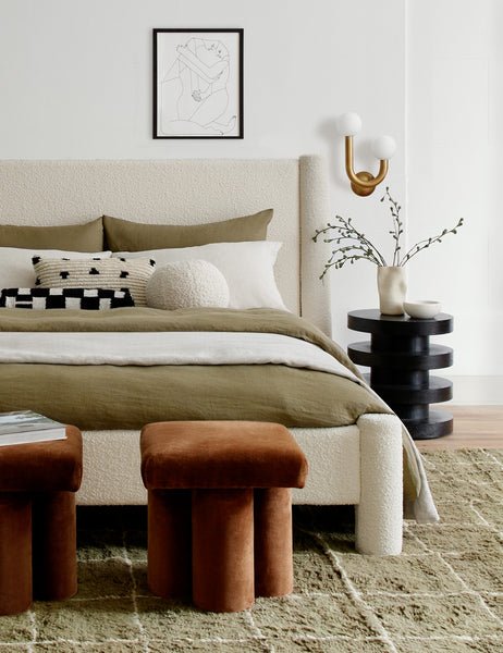 #showall::39723799248995 | Ivory Bouclé Ball Pillow by Sarah Sherman Samuel sits on a natural linen framed bed in a bedroom with a moss green rug and conganc ottomans