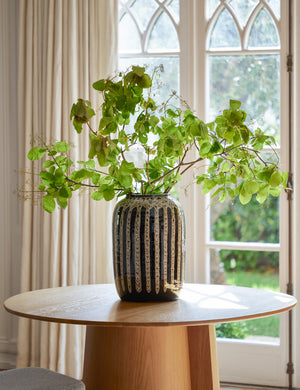 Wheaton full-bodied black and natural striped vase with a plant inside sits on a round wooden dining table with french doors in the background
