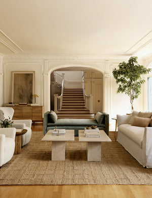 The Harper rug lays in a living room with accented walls under two stone coffee tables and ivory furniture