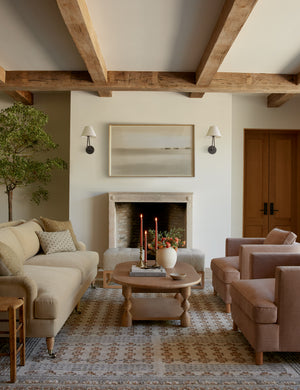  Two Hayden double-armed black sconce lights hang on both sides of a landscape painting in a living room with warm-toned furniture