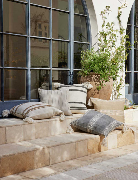 #color::camel | The Fez camel and white indoor and outdoor throw pillow sits on a stone staircase outside with other pillows