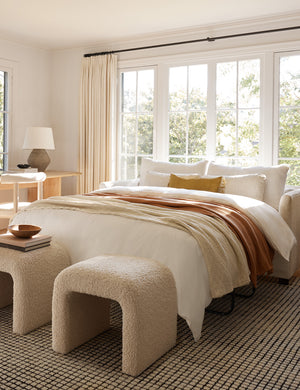 The Lotte White Basketweave queen-sized sleeper sofa with the bed pulled out sits atop a grid rug with two boucle ottomans