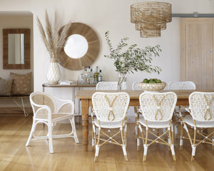The Minna three-tiered jute chandelier sits in a dining room with white woven dining chairs, a wooden dining table, and a jute framed circular mirror