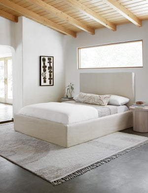 Canyon Terracotta Square Pillow sits on a neutral linen framed bed in a room with a black and white wall art and geometric tasseled rug